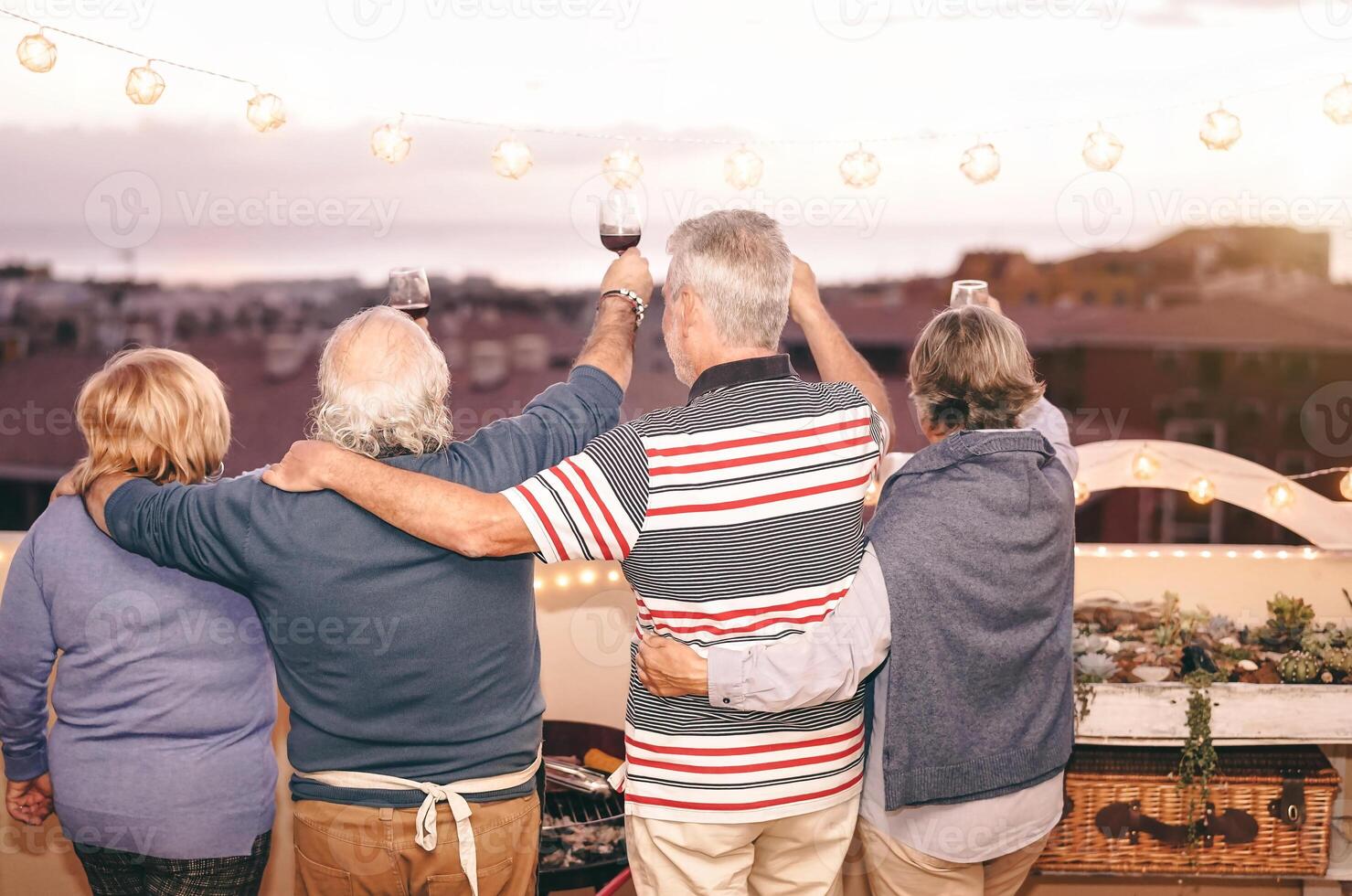 glücklich Senioren haben Spaß beim Dach Grill Party - - Alten Familie Essen und Jubel mit rot Wein Brille beim Grill auf Terrasse - - Menschen Lebensstil Essen und trinken Konzept foto