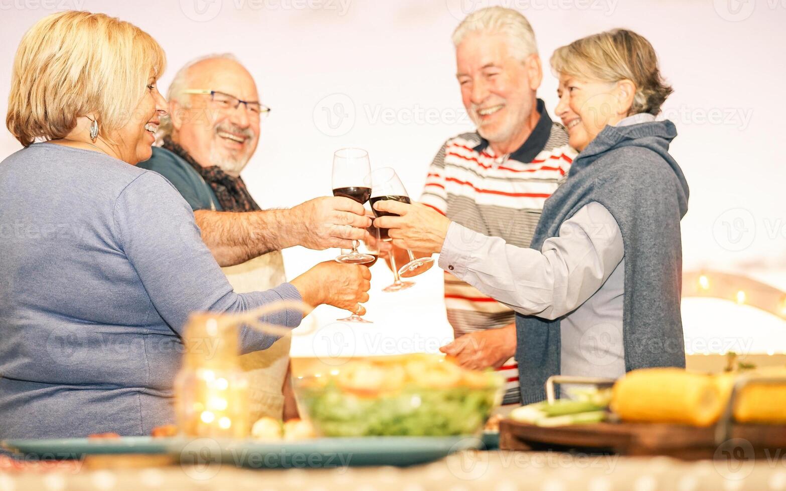 glücklich Senior freunde Toasten mit rot Wein beim Grill Abendessen im Terrasse - - reifen Menschen Essen und Jubel zusammen Trinken Wein auf Dach - - Freundschaft und Alten Lebensstil Konzept foto