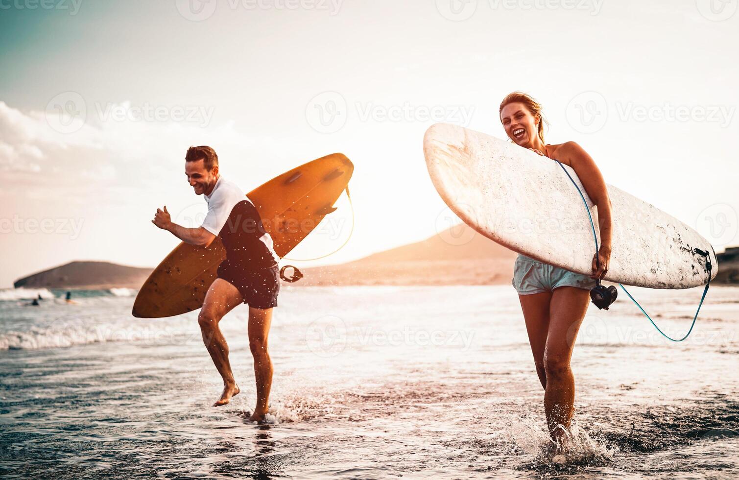 glücklich Surfer Paar Laufen mit Surfbretter entlang das Meer Ufer - - sportlich Menschen haben Spaß gehen zu Surfen zusammen beim Sonnenuntergang - - extrem Surfen Sport und Jugend Beziehung Lebensstil Konzept foto