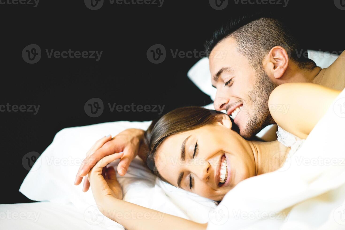 jung sexy Paar von Liebhaber Lügen auf Bett im ihr Flitterwochen - - jung bärtig Mann flüstert und küssen im schön Frau Ohr - - Liebe und Beziehung Konzept von ein Paar zusammen im Schlafzimmer foto