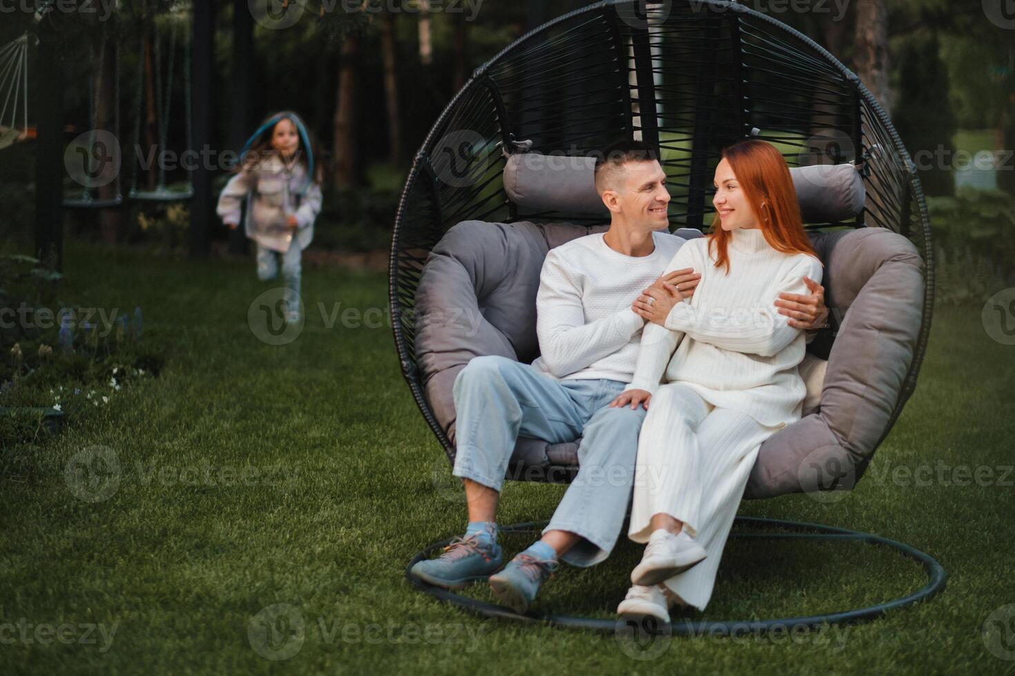 ein glücklich Familie ist Sitzung im ein Hängematte auf das Rasen in der Nähe von das Haus foto