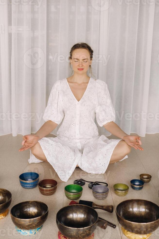 ein Frau sitzt mit tibetanisch Schalen im das Lotus Position Vor tun Yoga im das Fitnessstudio foto