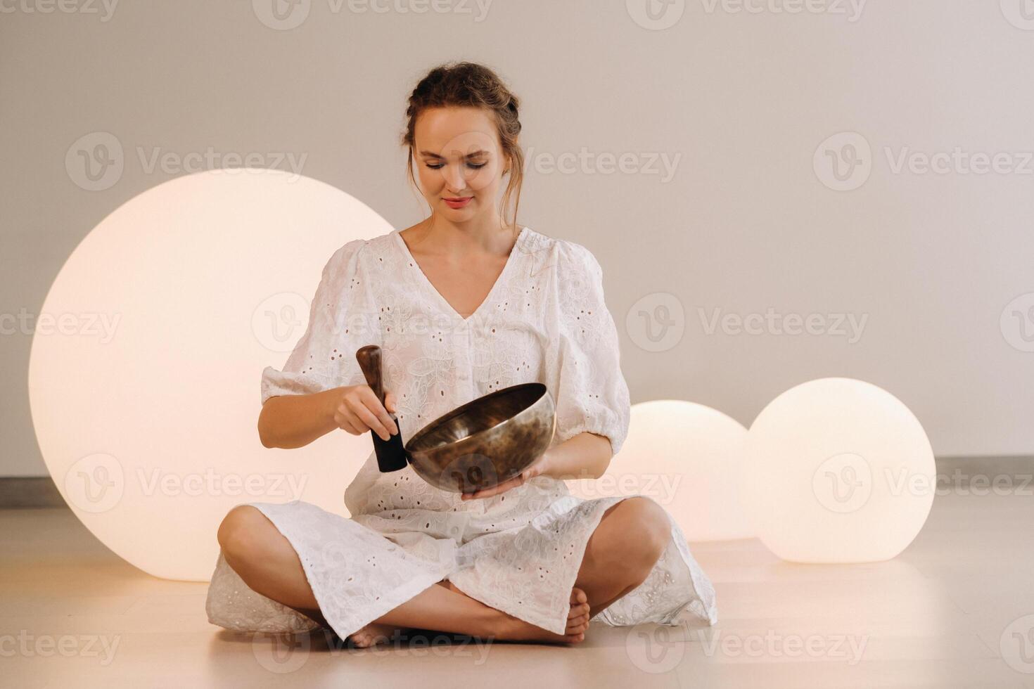 Porträt von ein weiblich Yoga Lehrer spielen ein tibetanisch Schüssel oder Singen ein Glocke im das Fitnessstudio während ein Yoga Rückzug foto