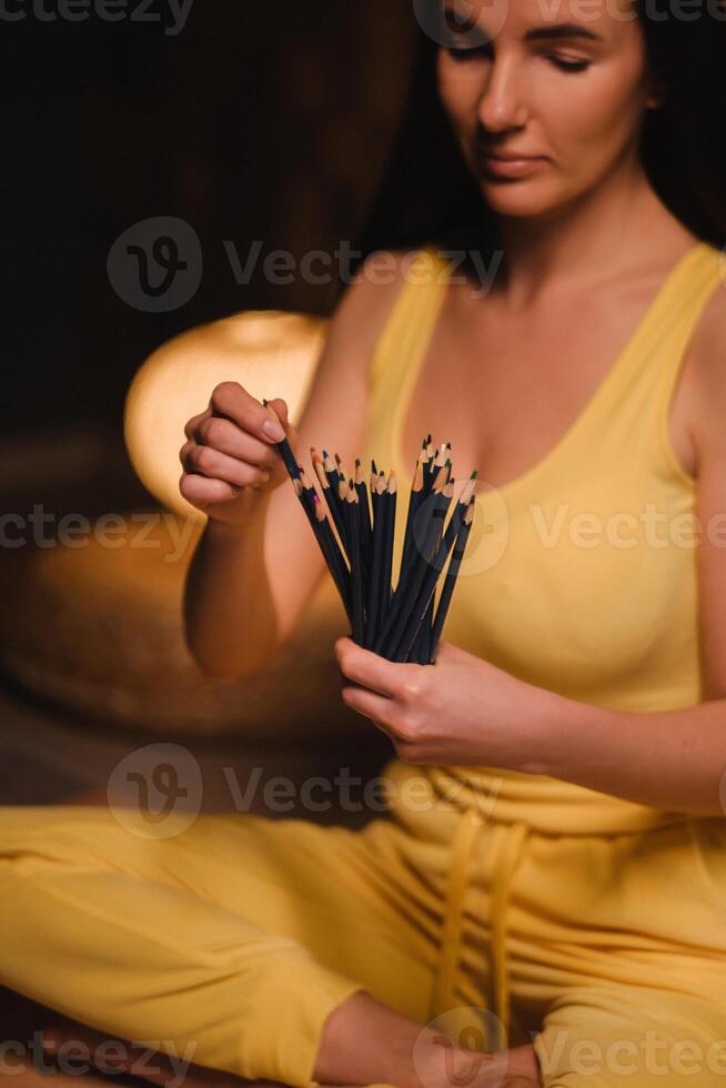 ein Mädchen im Gelb Kleider Sitzung auf das Fußboden halten Bleistifte zum Zeichnung foto