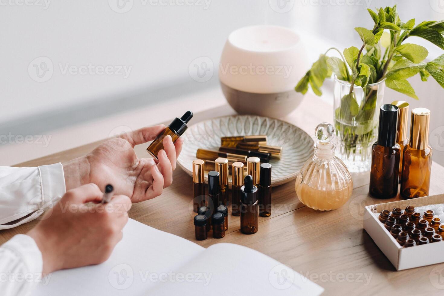 Nahansicht von weiblich Hände halten ein Flasche von wesentlich Öl und Schreiben ein Eintrag im ein Notizbuch, Aromatherapie foto