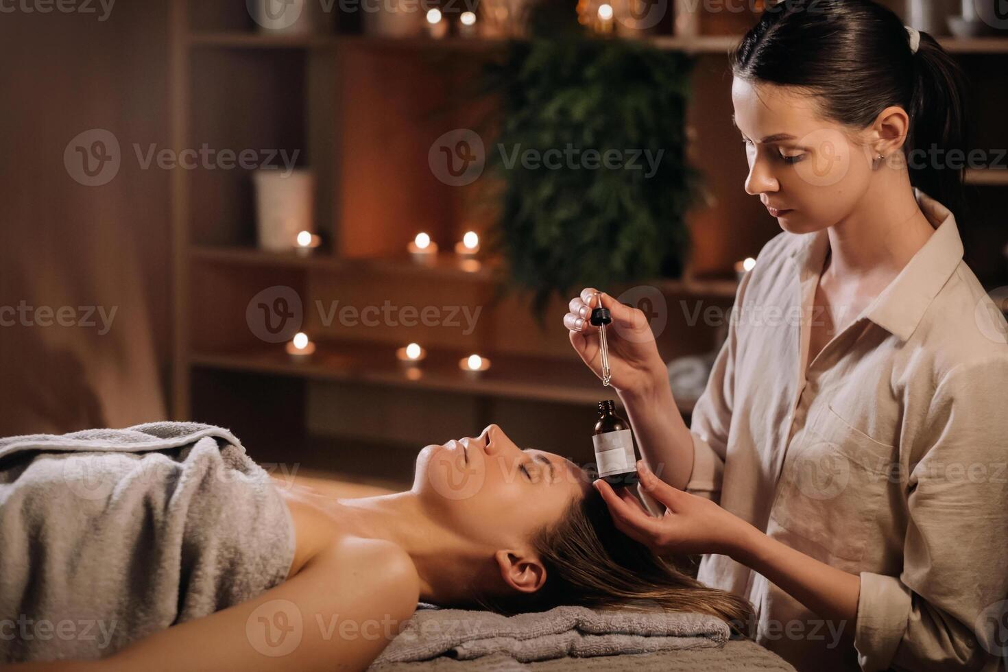 ein weiblich Kosmetikerin hält ein Pipette mit wesentlich Öl Vor Aromatherapie und Massage zu das geduldig. Aromatherapie foto