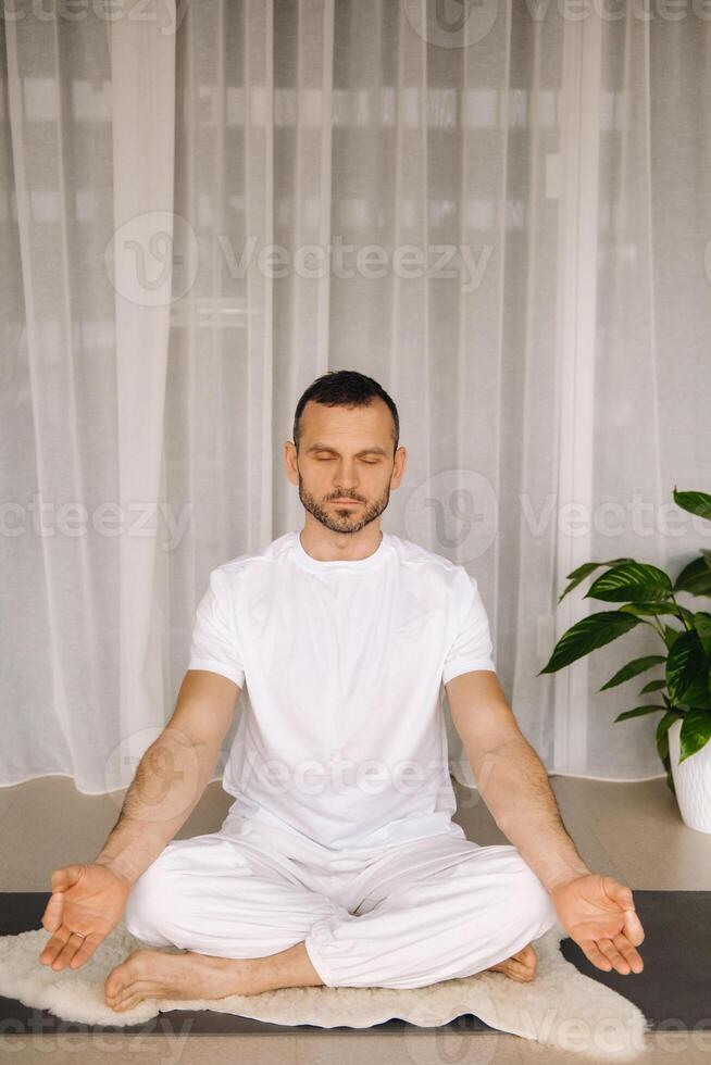 ein Mann im Weiß Sportbekleidung ist tun Yoga mit ein Fitness Zimmer. das Konzept von ein gesund Lebensstil foto