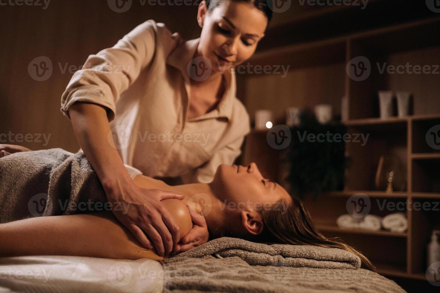 ein Masseuse gibt ein Körper Massage zu ein Frau im ein Spa Center. ein Fachmann Masseur Massagen das Schulter von ein Mädchen Lügen im ein Spa Center foto