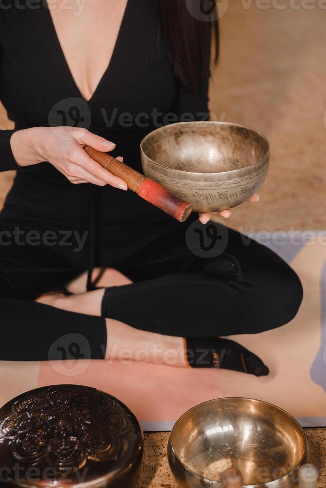 Nahansicht von ein Frau Hände Sitzung im ein Lotus Position mit ein Singen Schüssel drinnen. Entspannung und Meditation. Klang Therapie, Alternative Medizin. tibetanisch Schalen foto