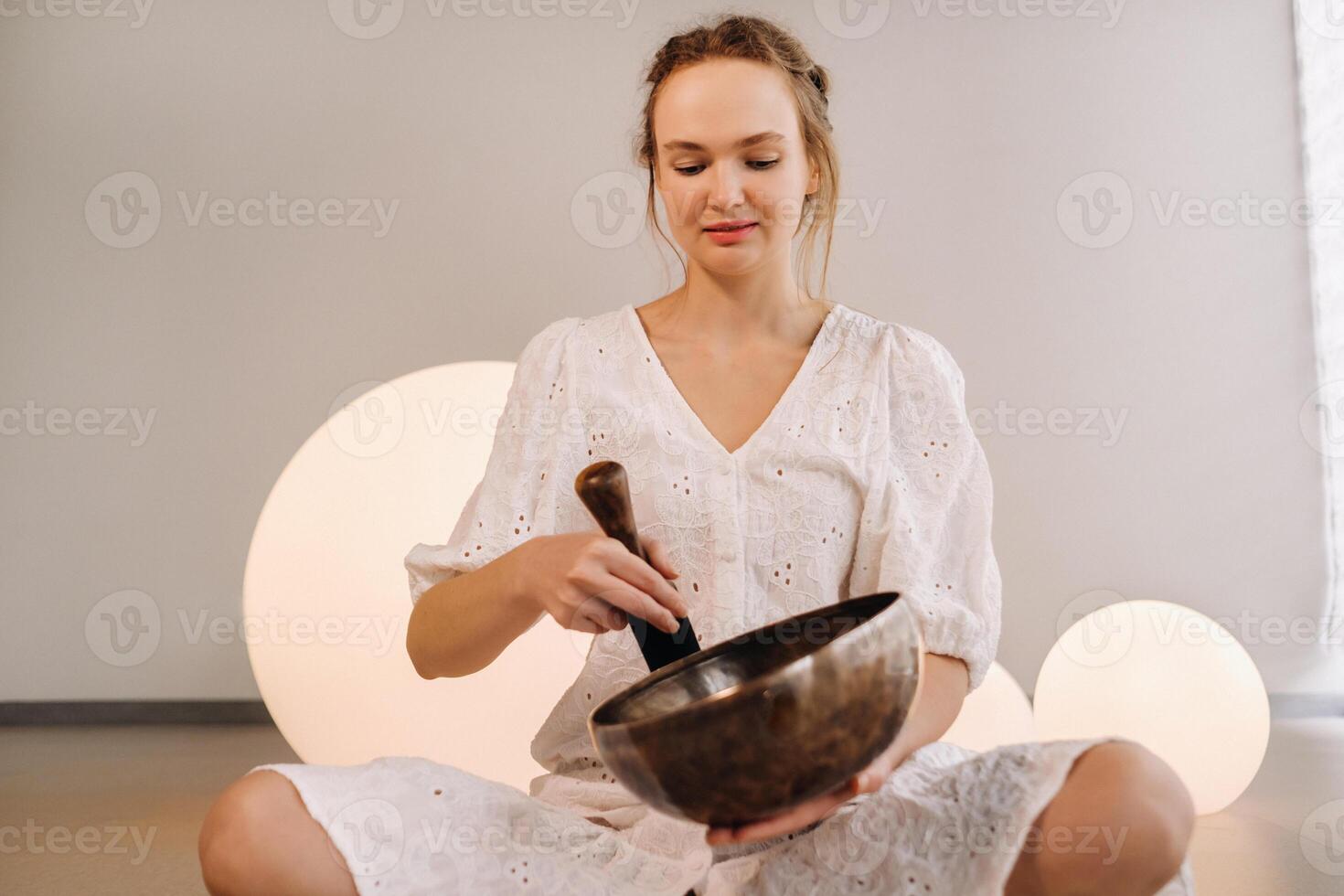 Porträt von ein weiblich Yoga Lehrer spielen ein tibetanisch Schüssel oder Singen ein Glocke im das Fitnessstudio während ein Yoga Rückzug foto