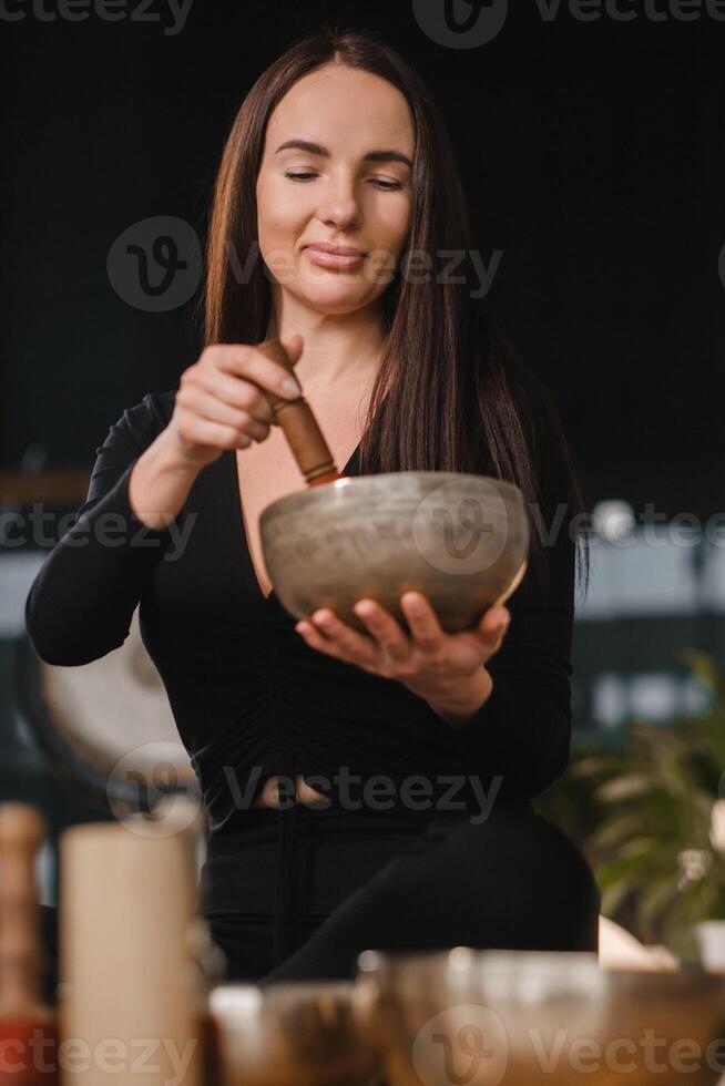 ein Frau im das Lotus Position mit ein Singen Schüssel drinnen . Entspannung und Meditation. Klang Therapie, Alternative Medizin. Buddhist Heilung Praktiken Methoden Ausübungen foto