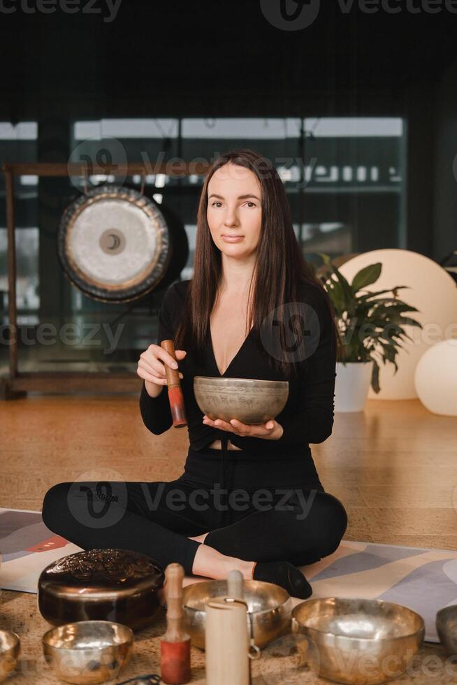 ein Frau im das Lotus Position mit ein Singen Schüssel drinnen . Entspannung und Meditation. Klang Therapie, Alternative Medizin. Buddhist Heilung Praktiken Methoden Ausübungen foto