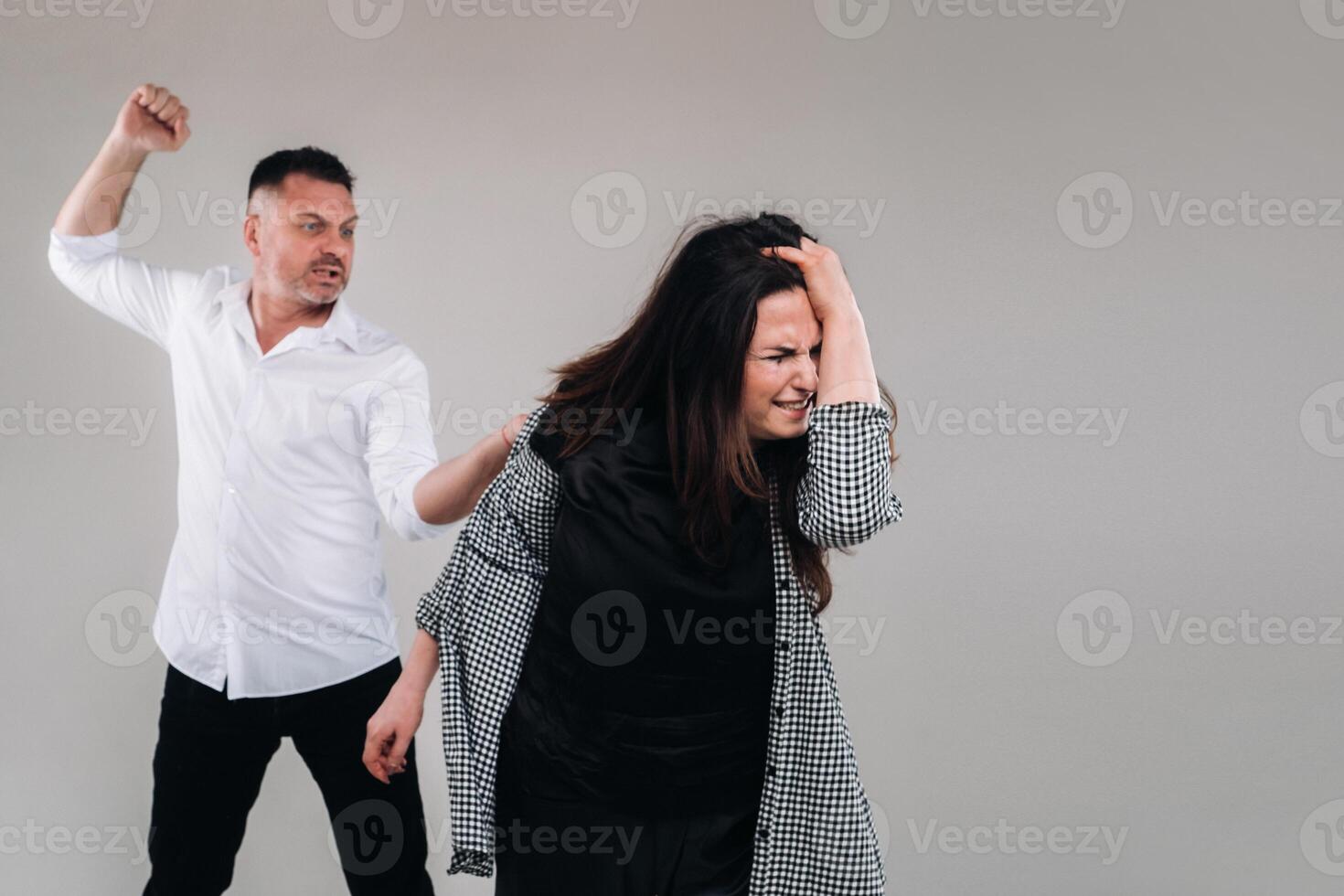 ein Mann Schaukeln seine Faust beim ein angeschlagen Frau Stehen auf ein grau Hintergrund. inländisch Gewalt foto