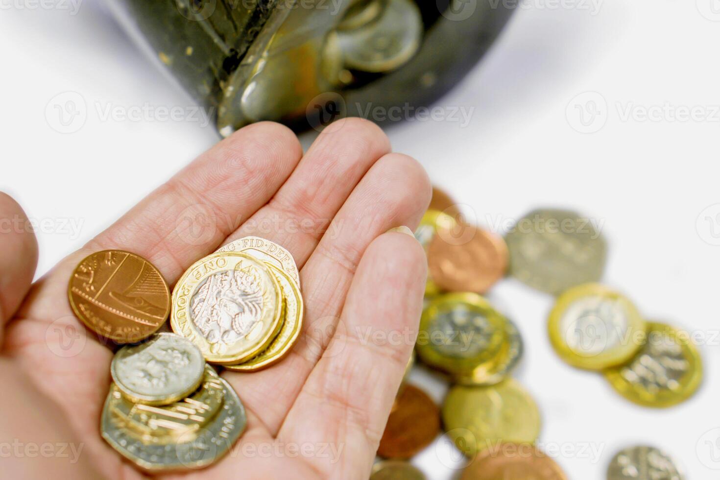 britisch Währung Münzen auf Hand und verschwommen Münzen öffnen von das Schweinchen Bank gelegt aus verstreut auf Weiß Hintergrund. foto