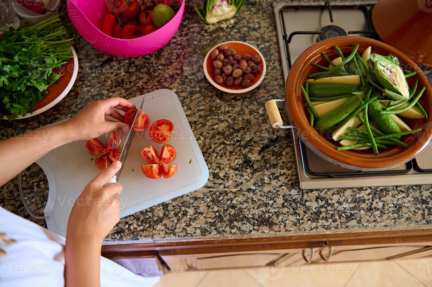 oben Aussicht von ein Hausfrau, Frau Koch halten ein Küche Messer, Hacken frisch saftig Tomaten auf ein Schneiden Tafel foto