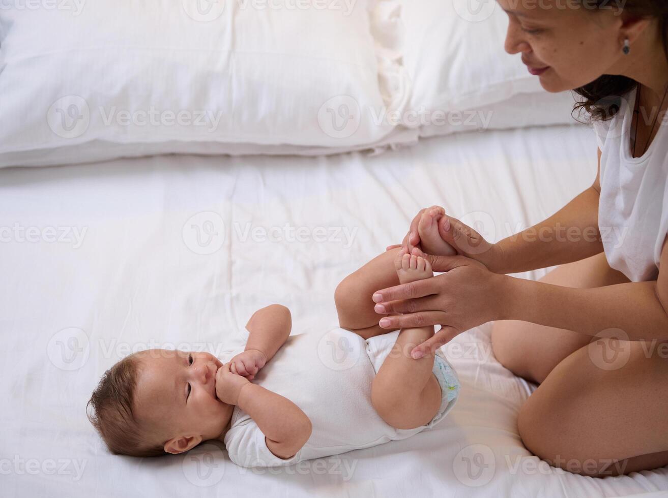 schön Neugeborene Baby Junge, sieht aus beim seine liebend Pflege Mutter streicheln und küssen seine wenig Füße und winzig Zehen. foto