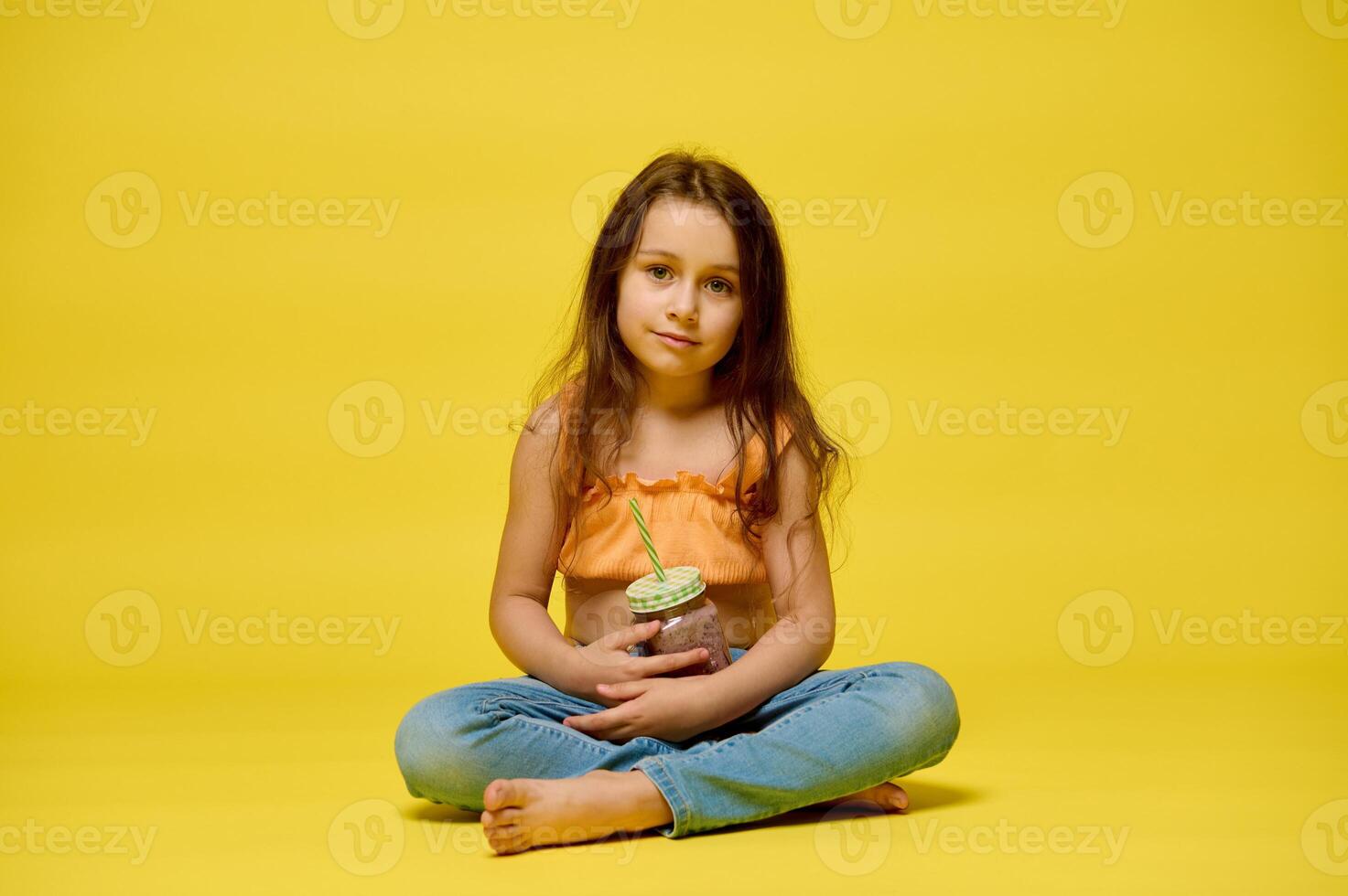komisch wenig Kind Mädchen mit ein Glas von Cocktail auf ein Gelb Hintergrund foto