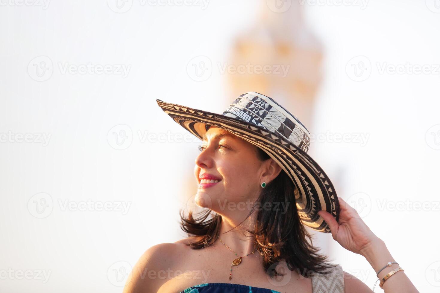 schön Frau tragen das traditionell kolumbianisch Hut namens Sombrero vueltiao beim das Uhr Turm auf das historisch Straßen von das Cartagena de Indien ummauert Stadt foto