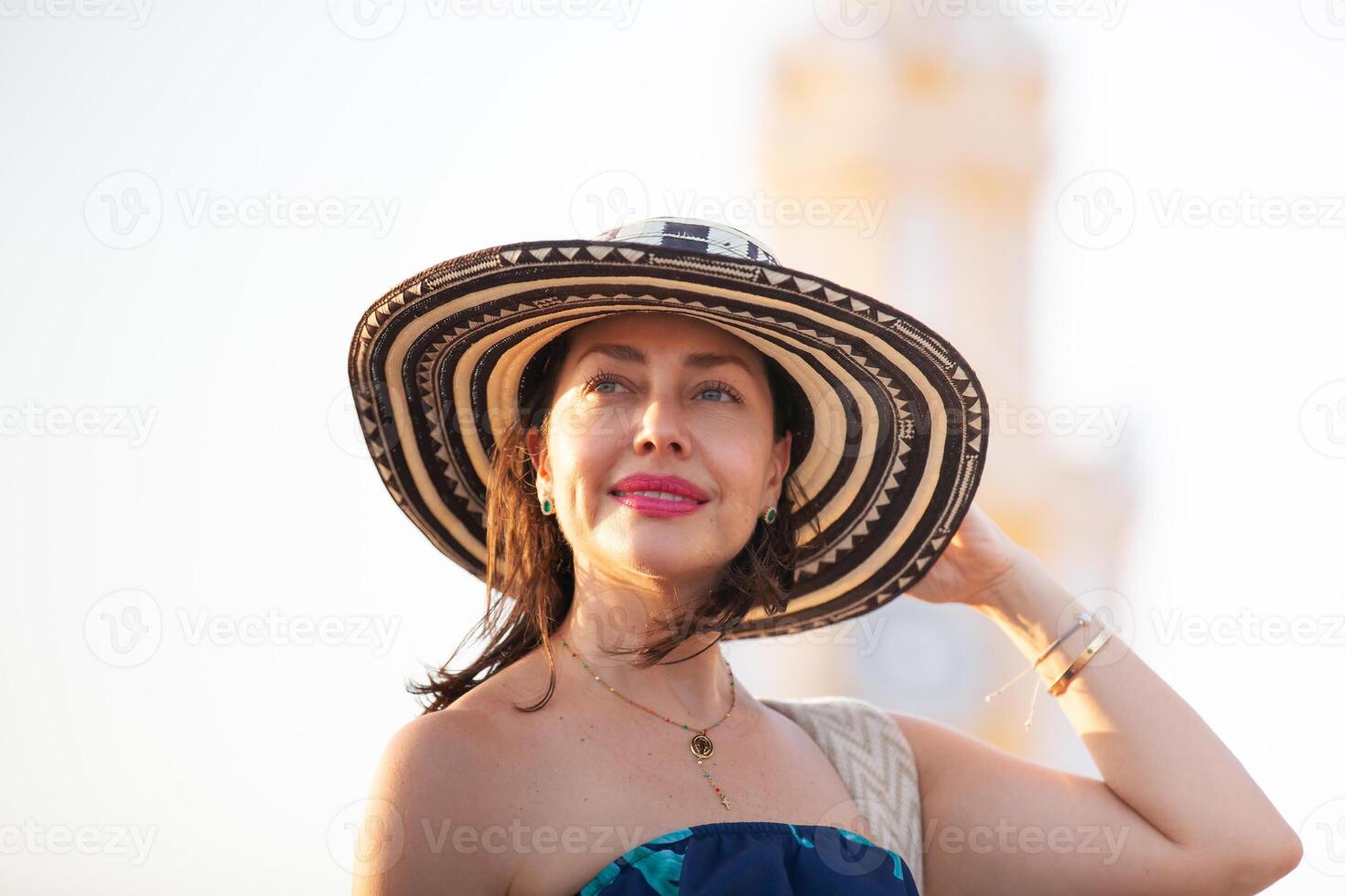 schön Frau tragen das traditionell kolumbianisch Hut namens Sombrero vueltiao beim das Uhr Turm auf das historisch Straßen von das Cartagena de Indien ummauert Stadt foto