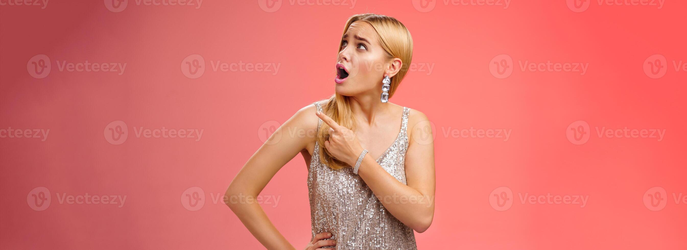 schockiert unzufrieden gestört arrogant blond Glanz Frau im Silber glänzend Kleid drehen Oberer, höher richtig Ecke zeigen sich beschweren seltsam Lärm Kommen Sie nach oben, Stehen in Frage gestellt rot Hintergrund foto