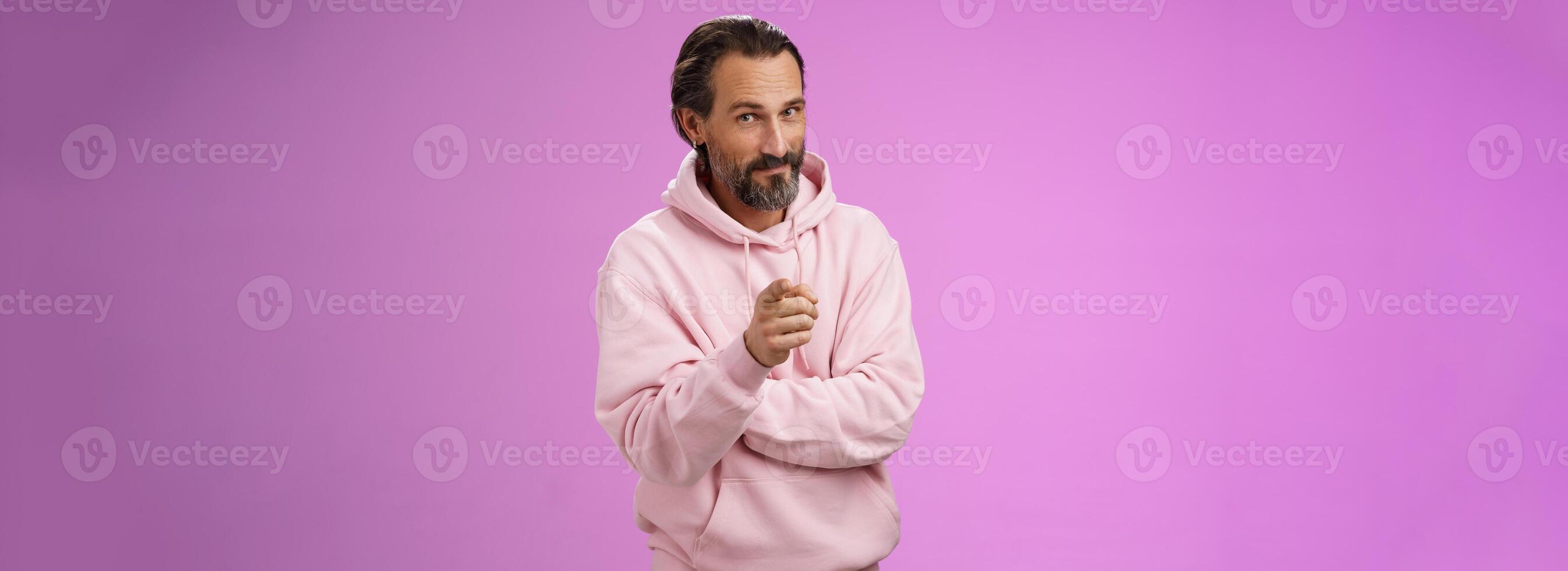 zuversichtlich gut aussehend charismatisch Erwachsene bärtig Mann im stilvoll Rosa Kapuzenpullover einladend Sie beitreten Unternehmen lächelnd selbstbewusst Anzeige pflücken machen Entscheidung wählen uns, lila Hintergrund foto