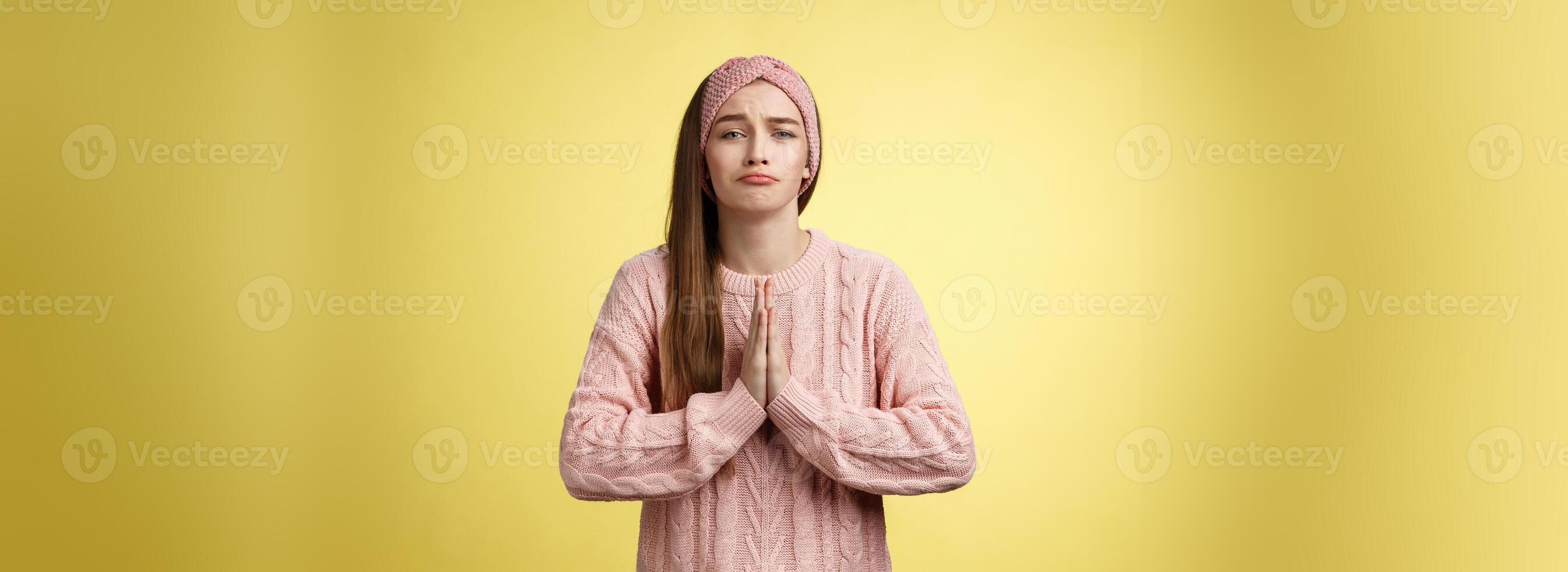 absichtlich traurig Mädchen im Sweatshirt drücken Palmen zusammen im beten schmollen beten zum Hilfe, fragen favorisieren, betteln Freund verleihen süß Kleid zum Datum, lächelnd albern, wollen etwas Über Gelb Hintergrund foto