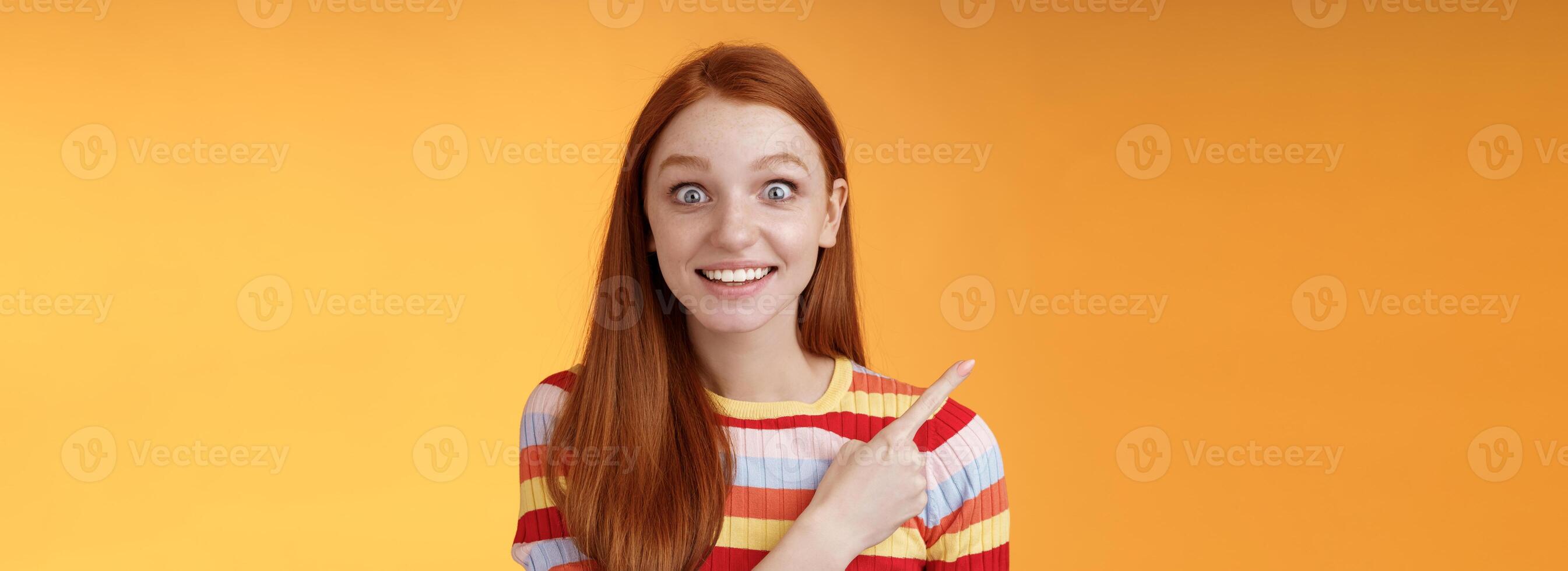 aufgeregt begeistert gut aussehend jung dumm Rothaarige Mädchen überrascht Pop Augen Kamera keuchend beeindruckt zeigen Oberer, höher links Ecke sehen Super Star grinsend Aufregung Freude, Orange Hintergrund foto