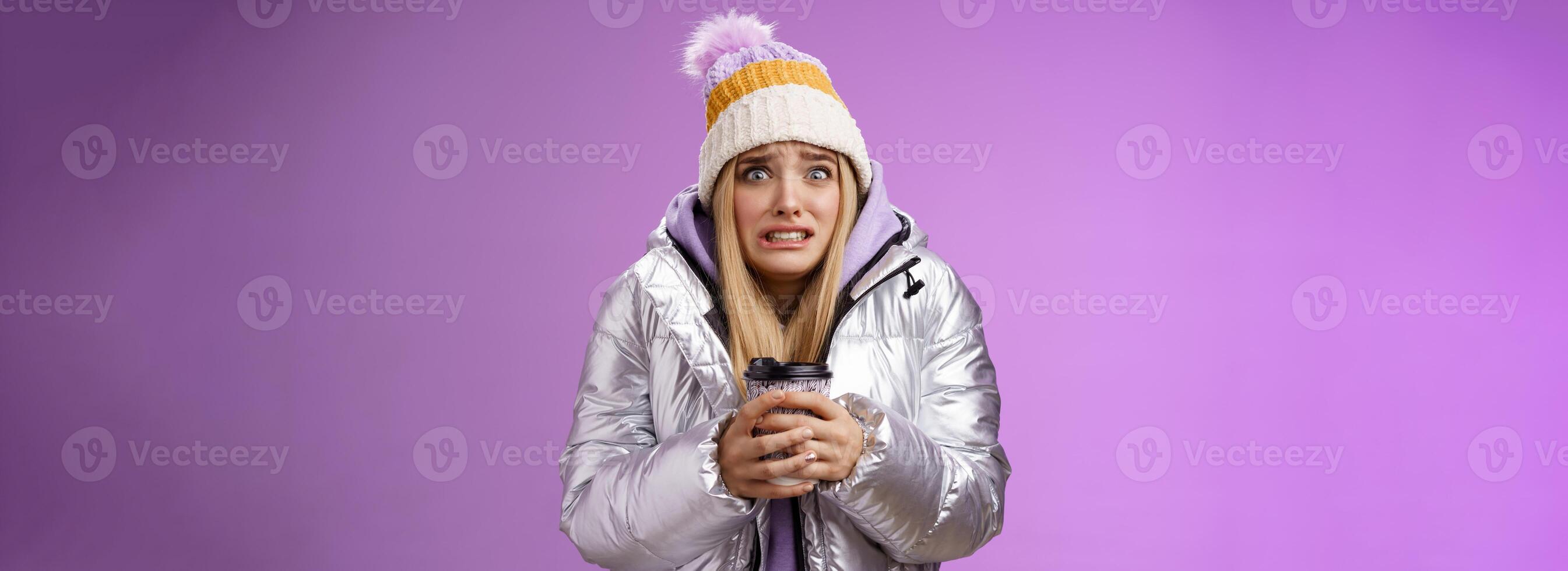 zittern unbequem unzufrieden Mädchen tragen stilvoll Silber Jacke Hut Zittern Einfrieren kalt warm Hände halten wegbringen Kaffee Tasse ballen Zähne Pop Augen leichte Schmerzen, Stehen lila Hintergrund foto