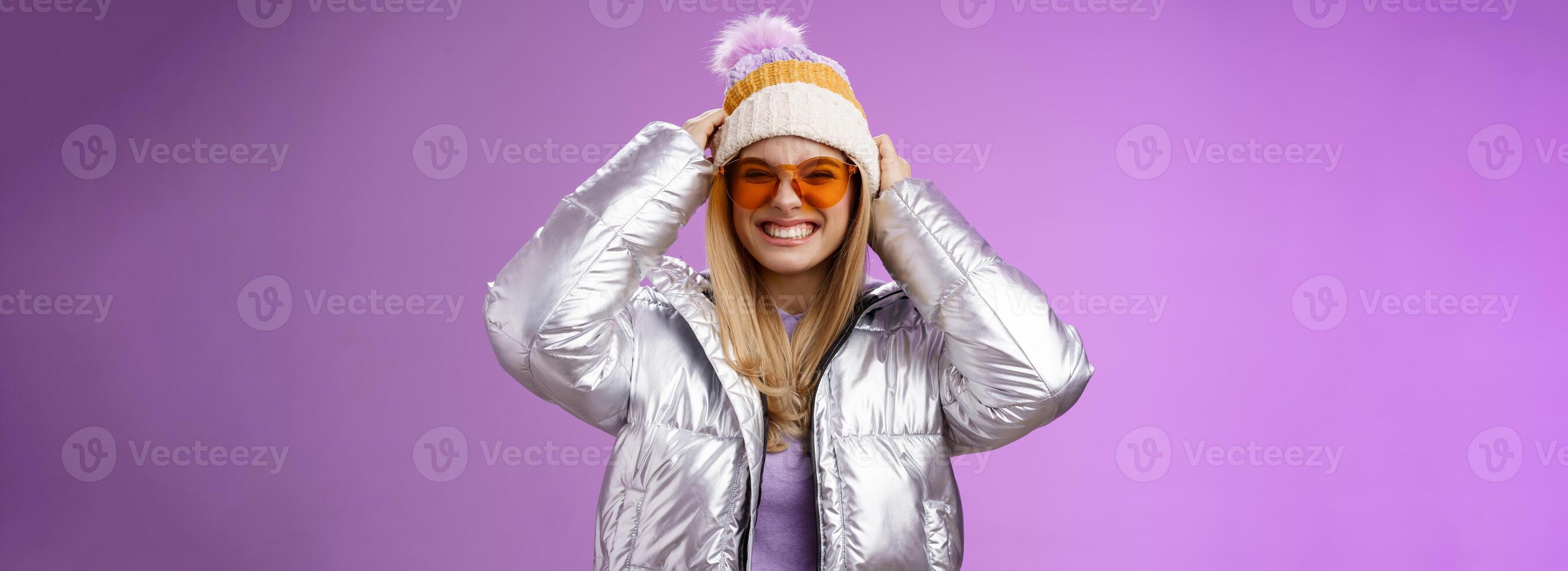 erregt gewagt frech jung attraktiv Frau haben Spaß freunde Winter Ausflug lernen Snowboarden lächelnd frech genießen Ferien aufsetzen Hut tragen Silber warm Jacke Sonnenbrille, lila Hintergrund foto