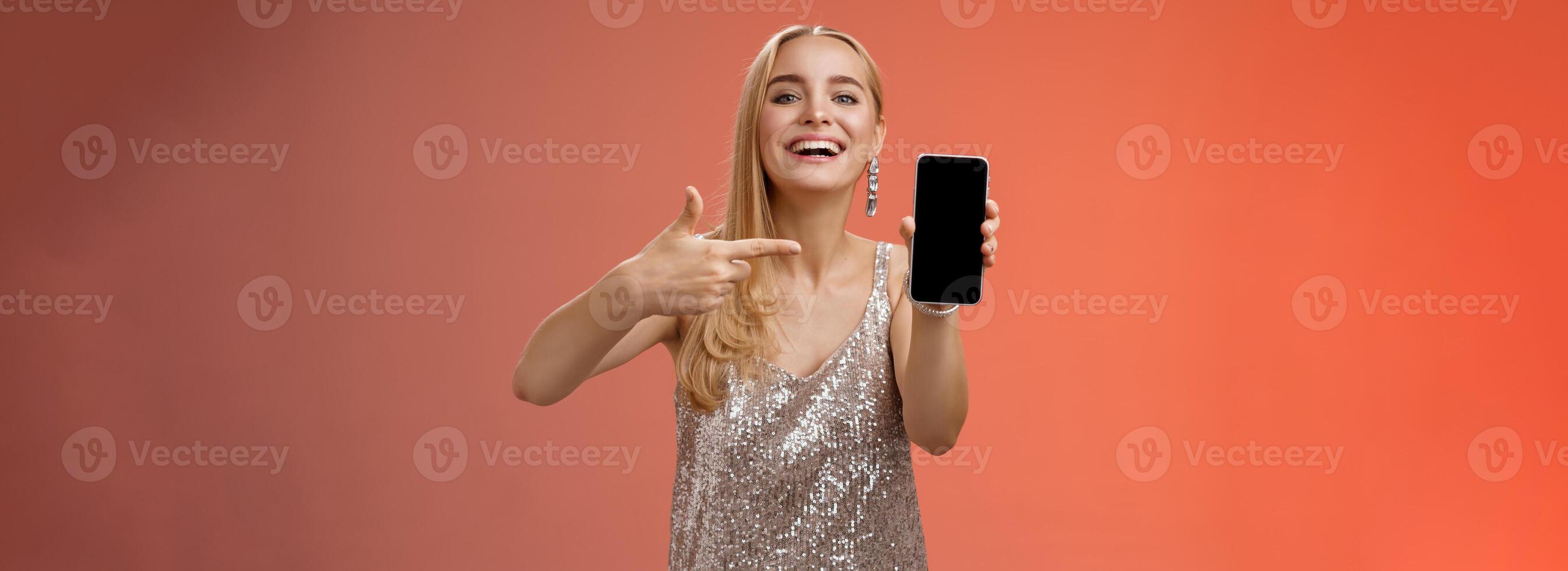prahlerisch stolz charmant elegant blond Frau im stilvoll Abend Kleid Show Smartphone Anzeige stolz zeigen Handy, Mobiltelefon Telefon Bildschirm lächelnd zeigen Foto Freund, Stehen rot Hintergrund