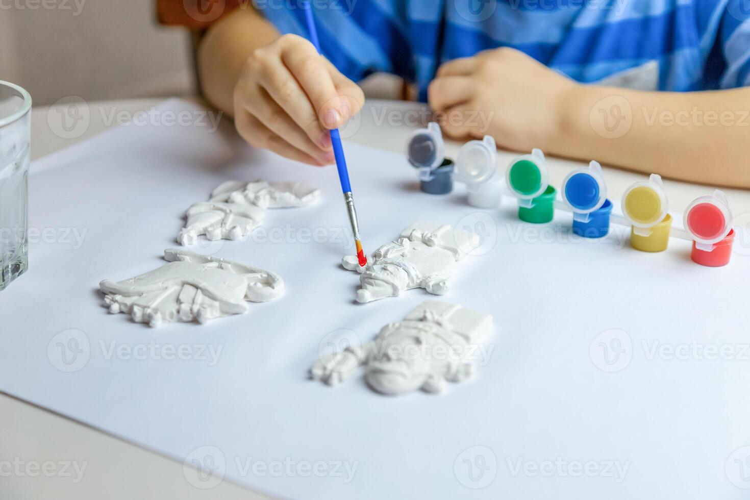 das Kind zeichnet und Farben Gips zahlen mit ein Bürste und Gouache auf ein Stück von Papier. foto