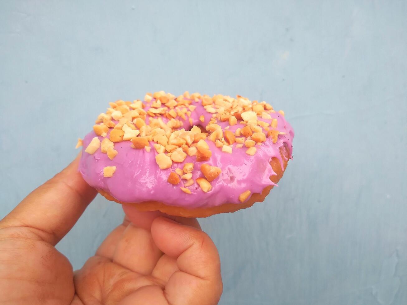 weiblich Hand hält ein Krapfen auf ein Blau Hintergrund. Konzept Süßwaren speichern, Gebäck, Kaffee Geschäft. Banner. eben legen, oben Sicht. foto