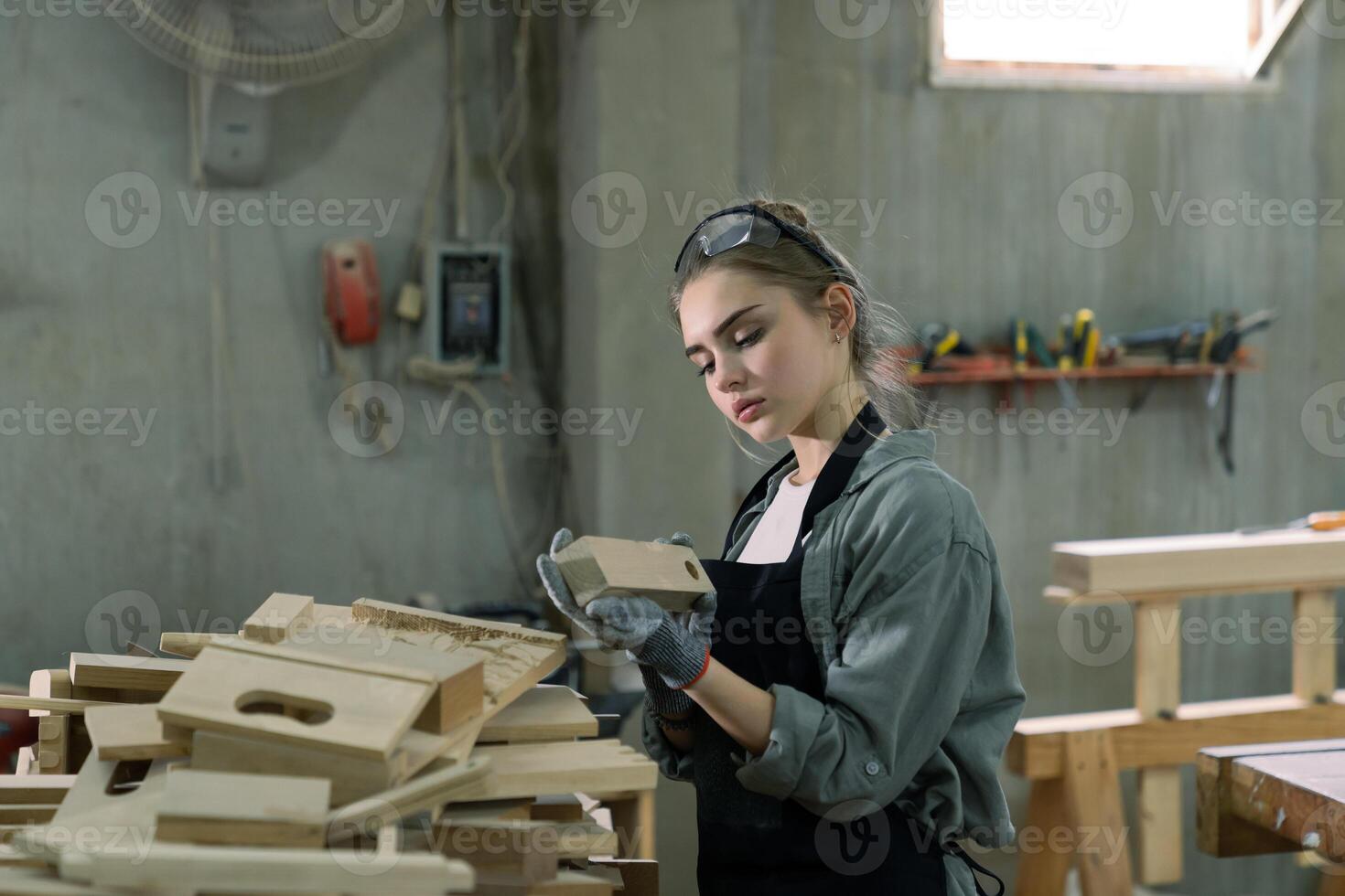 ein jung Frau ist Ausbildung zu Sein ein Zimmermann im das Werkstatt. sie funktioniert mit ein Laptop Computer im ein Holz Werkstatt. weiblich Zimmermann Kontakt Kunden durch Smartphone. sme Aufträge, Start-ups und klein foto