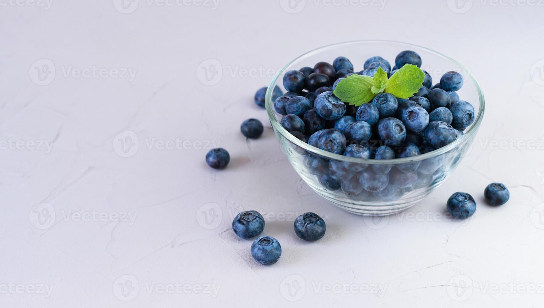 frisch gepflückt Blaubeeren im ein Glas Schüssel auf grau Hintergrund. Nahansicht. Platz zum Text. foto