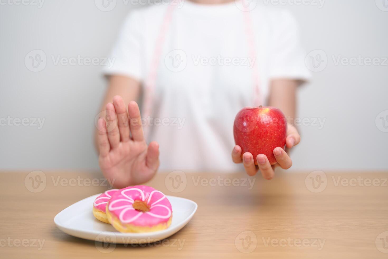 Frau Hand halt rot Apfel und ablehnen Krapfen, weiblich Fitness wählen zwischen Obst ist gesund und Süss ist ungesund Müll Lebensmittel. Diät Kontrolle, Gewicht Verlust, Fettleibigkeit, Essen Lebensstil und Ernährung foto