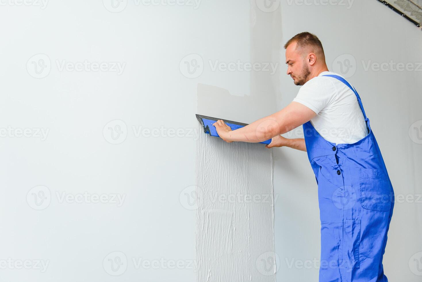 ein Allgemeines Arbeiter im Overall Verwendet ein Kelle zu Startseite das Mauer mit Zement foto