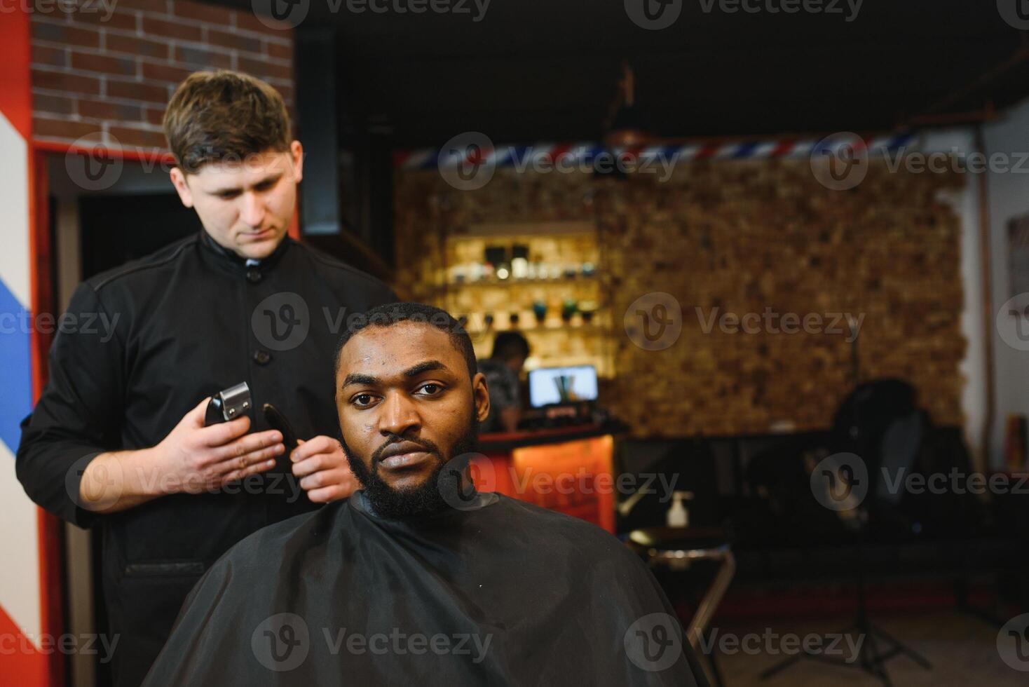 Nahansicht von Prozess von Trimmen von Haar im Barbier Geschäft. qualifiziert Barbier behalten Clipper im Hände und korrigieren gestalten von Haar zu männlich Klient Sitzung auf Stuhl. Konzept von Haarschnitt und Rasieren. foto