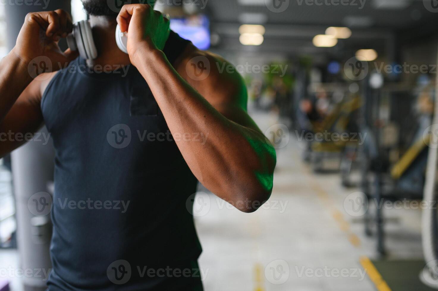 sportlich Mann Stehen im ein Fitnessstudio Hören zu Musik- mit kabellos Kopfhörer foto