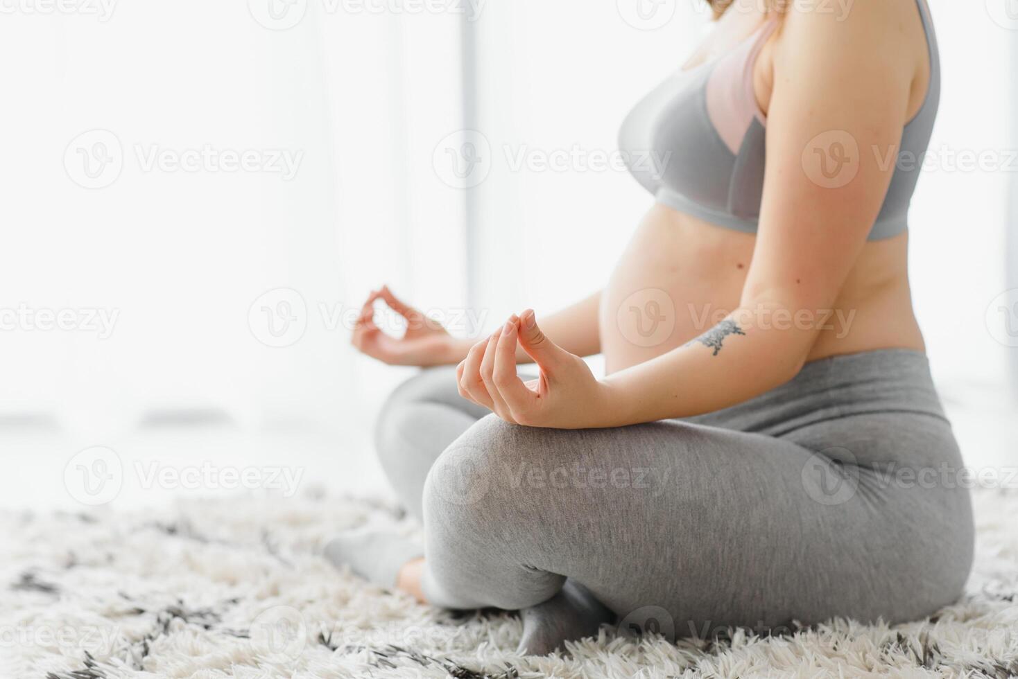 Nahansicht Schuss von unkenntlich schwanger Frau meditieren beim heim, erwartungsvoll Dame Sitzung im Lotus Position mit umklammert Hände, üben Yoga zum gesund Schwangerschaft, abgeschnitten Bild mit kostenlos Raum foto