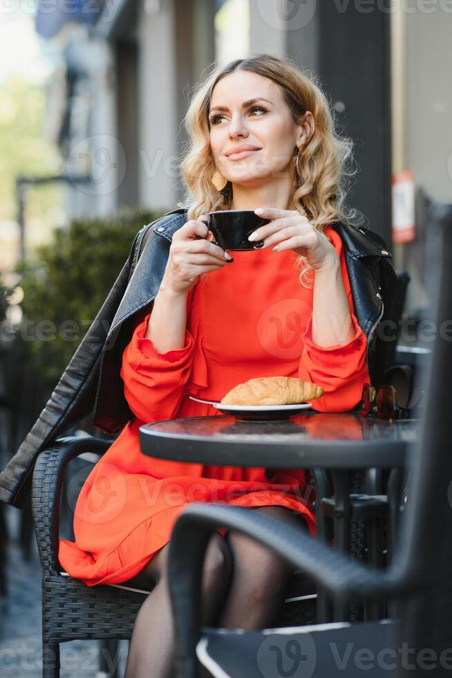 Mode Porträt von jung Frau Standort beim das Tabelle mit Tasse von Kaffee, Tee im Straße Cafe. foto