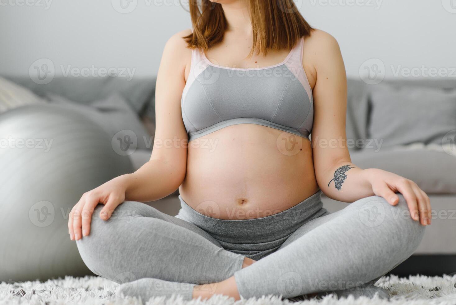 Nahansicht Schuss von unkenntlich schwanger Frau meditieren beim heim, erwartungsvoll Dame Sitzung im Lotus Position mit umklammert Hände, üben Yoga zum gesund Schwangerschaft, abgeschnitten Bild mit kostenlos Raum foto