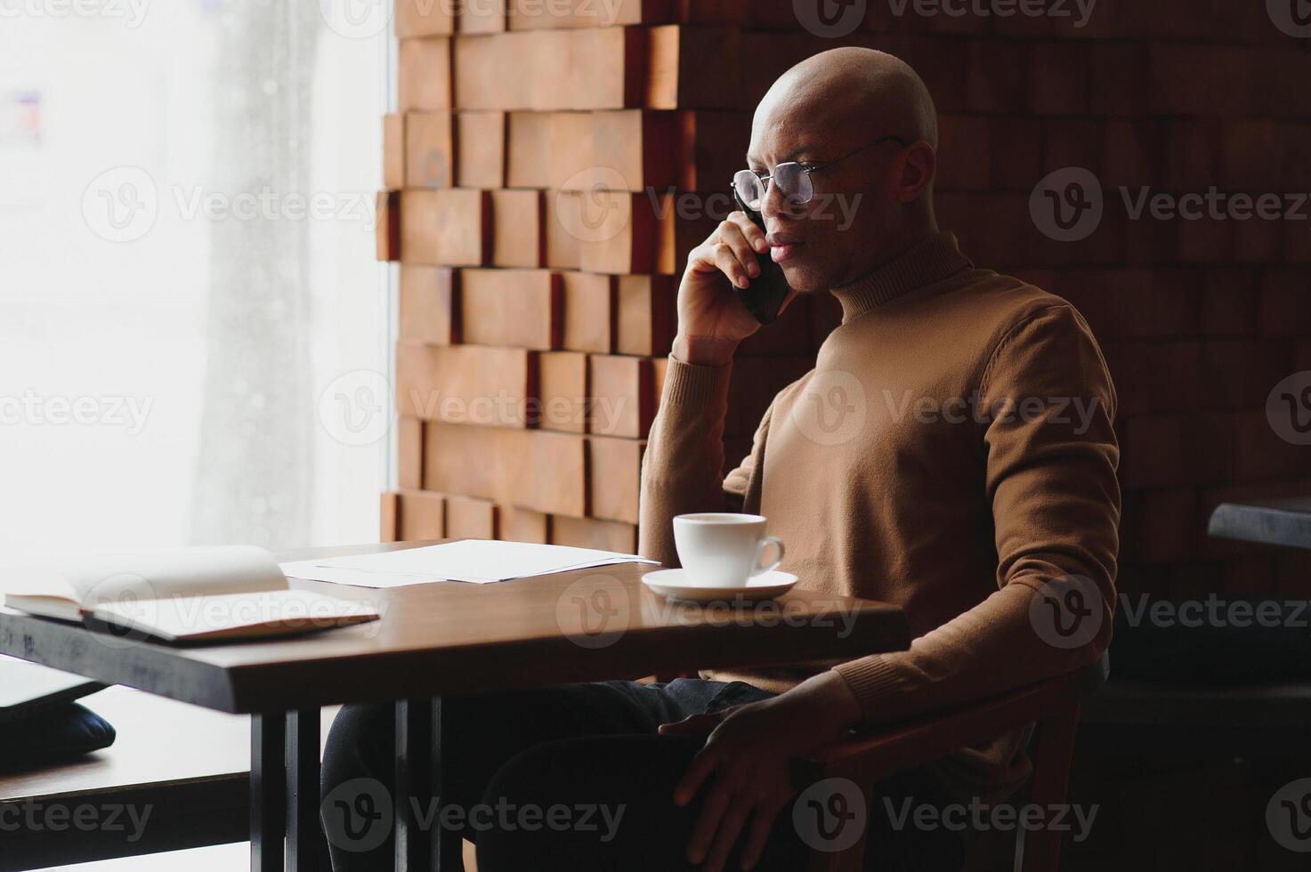 konzentriert schwarz männlich Unternehmer liest Papier Unterlagen Sitzung im Cafe mit Kaffee in der Nähe von Fenster. foto