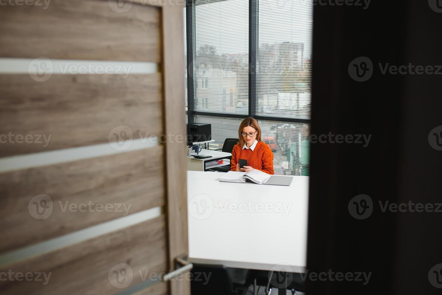 Porträt von ein glücklich beiläufig Geschäftsfrau im Sweatshirt Sitzung beim ihr Arbeitsplatz im Büro foto