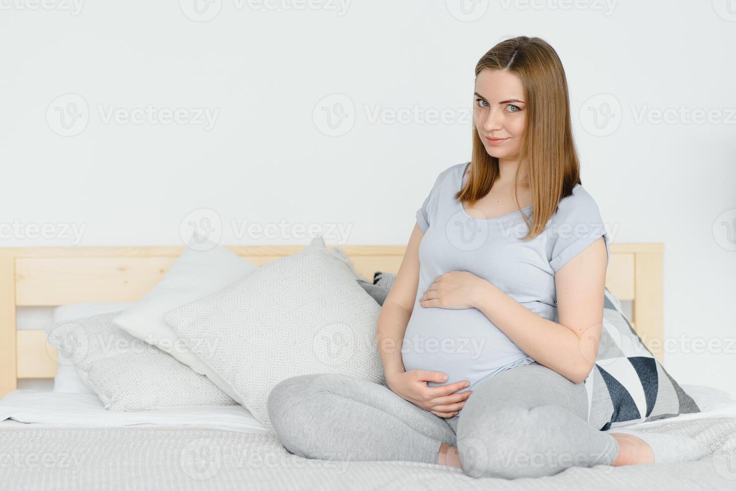 schwanger jung europäisch Frau Sitzung auf ein groß Bett und streicheln ihr groß Bauch, 7 Monat Schwangerschaft, warten zum das Geburt von ihr Baby. foto