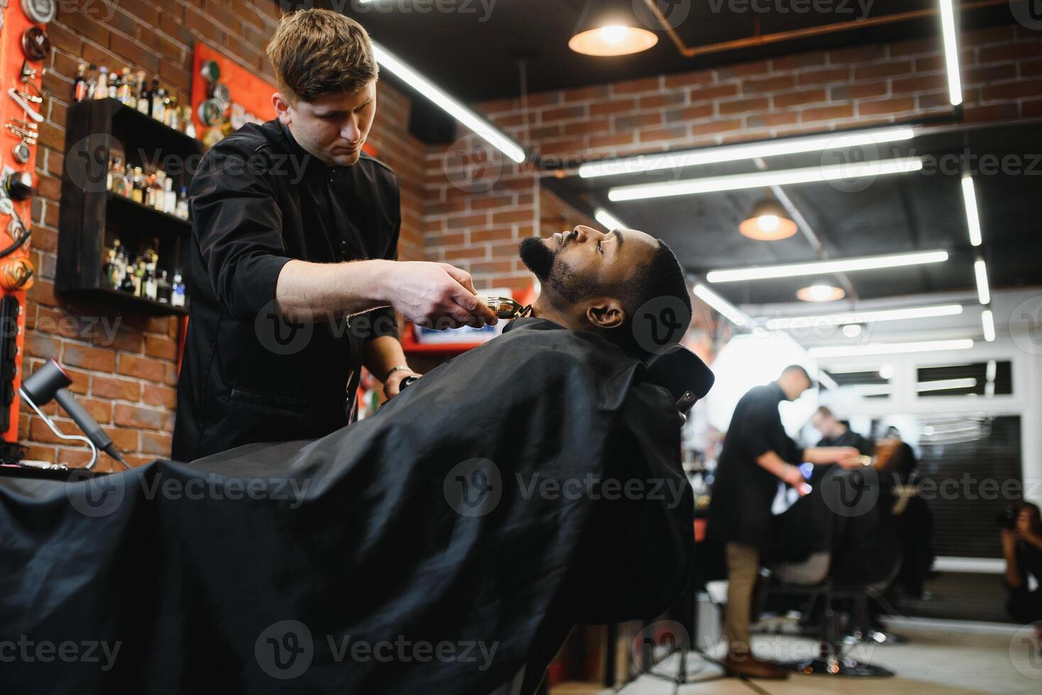 ein Barbier ist gehen durch das elektrisch Schneiden und Rasieren Maschine zum das Bart von ein Afroamerikaner Brasilianer Junge. foto