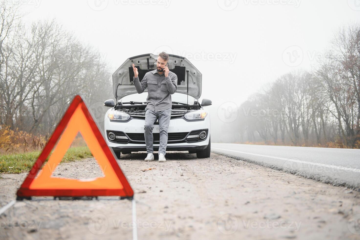 traurig Mann auf das Straße Nächster zu das gebrochen Auto foto