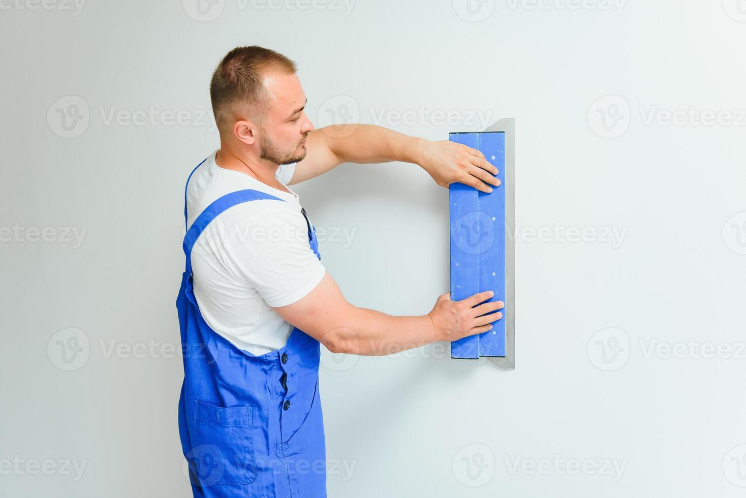 Porträt von ein Arbeiter im Overall und halten ein Kitt Messer im seine Hände gegen das verputzt Mauer Hintergrund. Reparatur Arbeit und Konstruktion Konzept foto