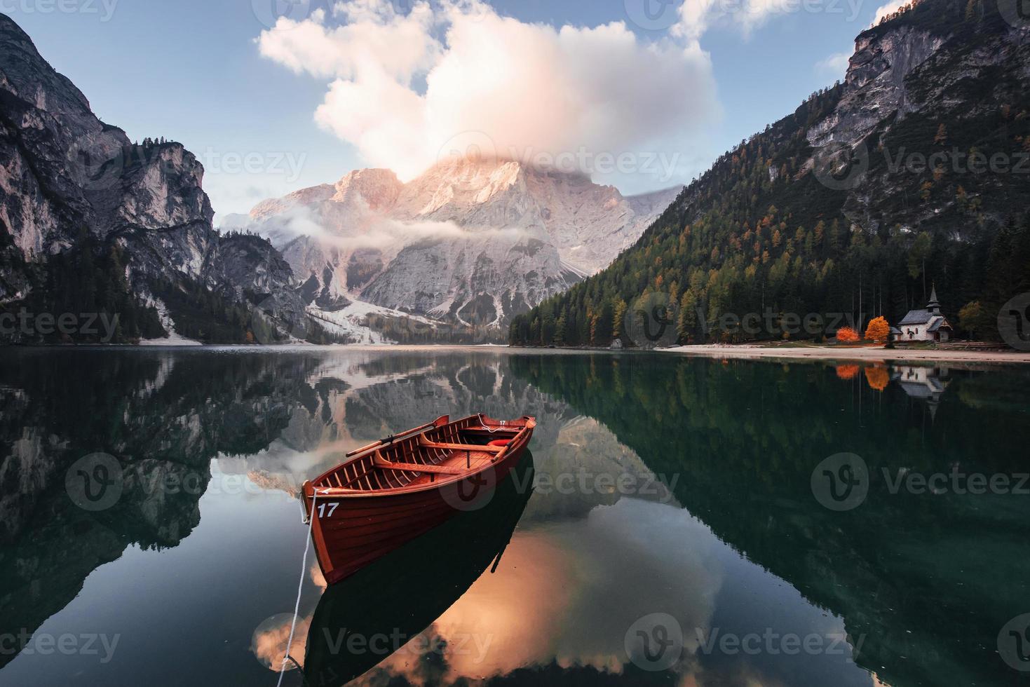 herrliche Landschaft. Holzboot auf dem Kristallsee mit majestätischem Berg dahinter. Spiegelung im Wasser. Kapelle ist an der rechten Küste foto