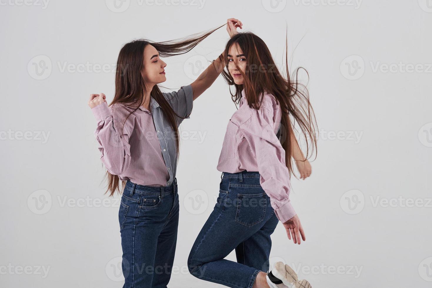 mit den Haaren spielen. zwei Schwestern Zwillinge stehen und posieren im Studio mit weißem Hintergrund foto
