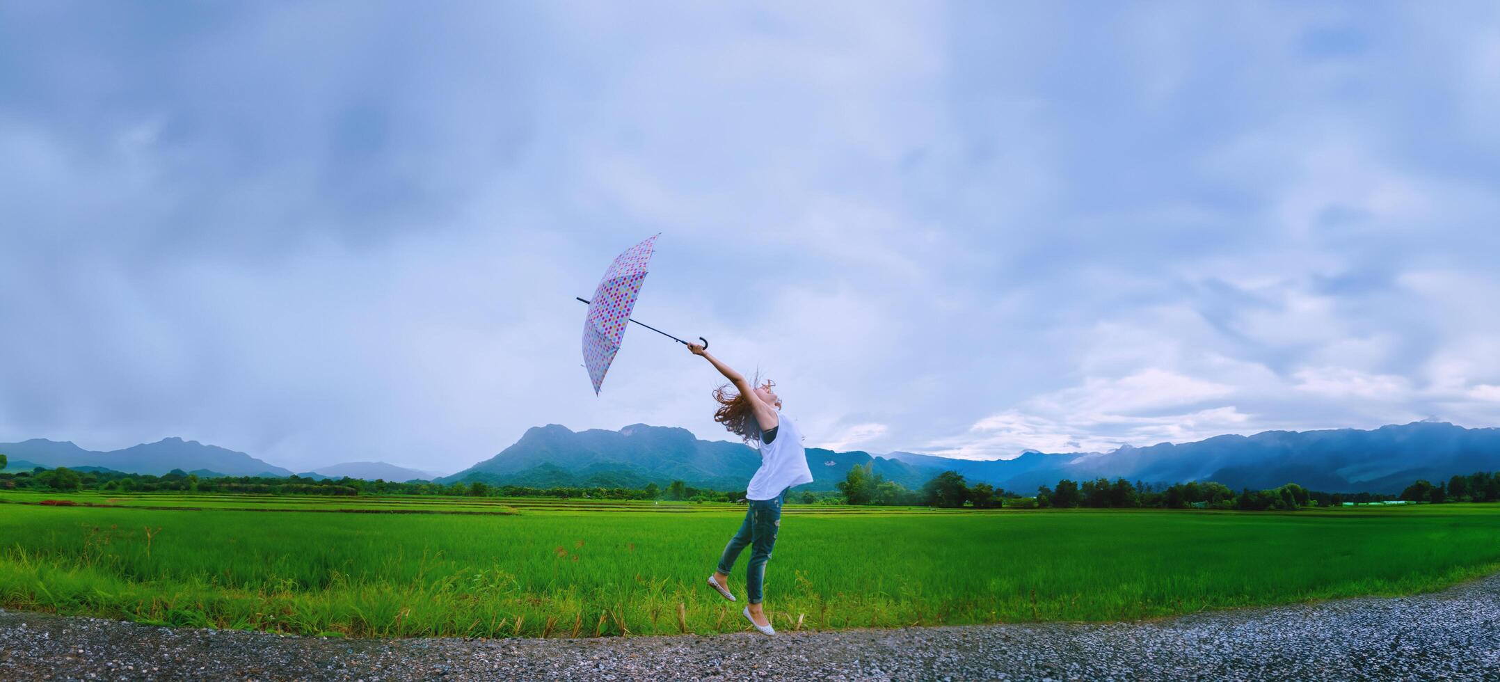 asiatische frauen reisen im urlaub entspannen. Die Frauen standen glücklich mit einem Regenschirm im Regen und genießen den Regen, der fällt. Reisen in Länder, grüne Reisfelder, Reisen durch Thailand. foto